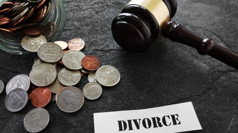 Glass jar with scattered coins, wooden judge's gavel, and paper labeled "DIVORCE" on black surface.