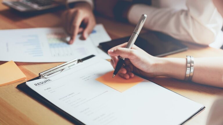 Close-up of hands reviewing a resume and pointing at a document on a wooden desk.