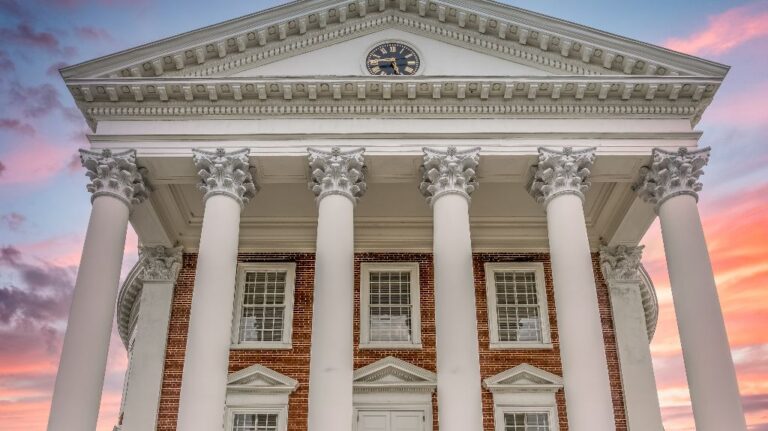 Neoclassical building facade with Corinthian columns, clock, and sunset sky background.