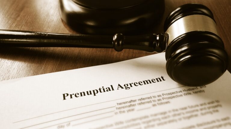 Close-up of a wooden gavel resting on a prenuptial agreement document on a wooden desk.