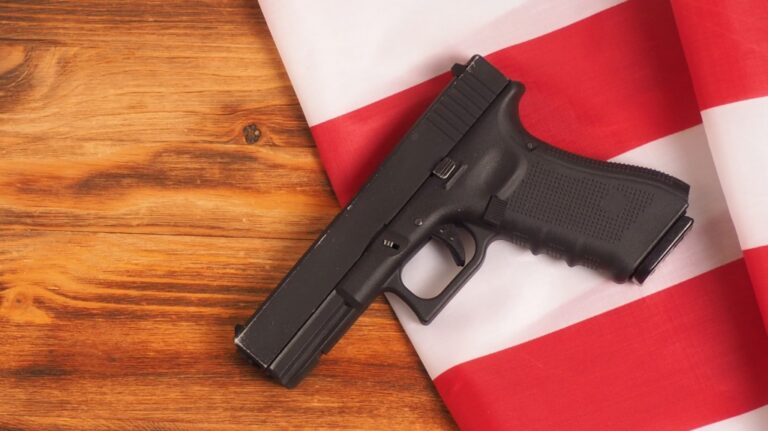 Black semi-automatic handgun resting on folded red and white striped fabric on wooden surface.