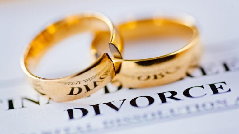 Two broken gold wedding rings placed on a document with the word "DIVORCE" prominently visible.