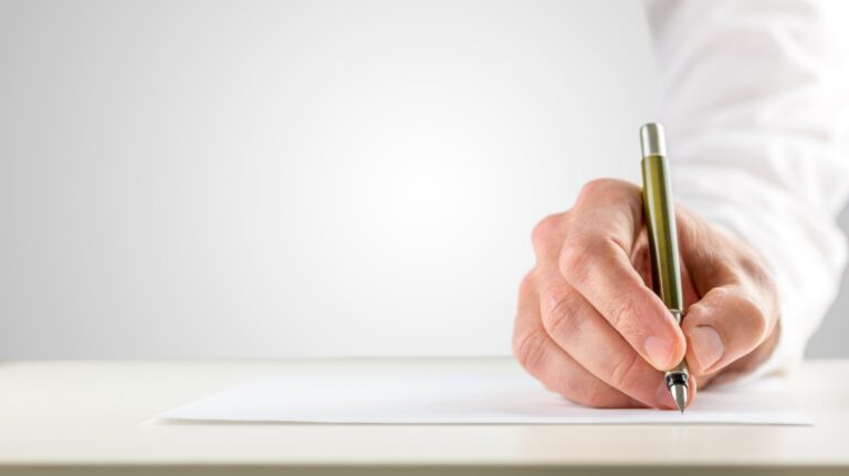Close-up of a hand holding a green pen poised to write on a blank white sheet of paper.