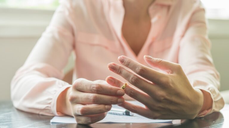 Woman in pink blouse removing a gold ring from her finger indoors.