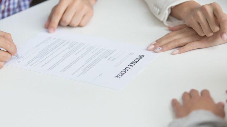 Two individuals reviewing and signing a divorce decree document on a white table.