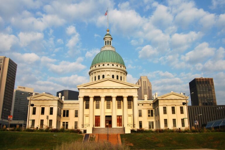 Historic neoclassical courthouse with green dome and American flag, surrounded by modern skyscrapers.