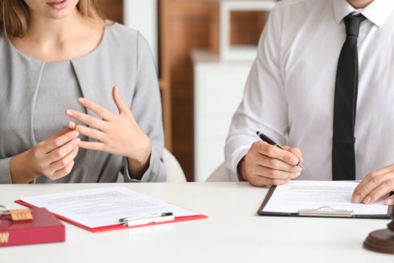 Woman removing wedding ring during consultation with man in white shirt and black tie at desk