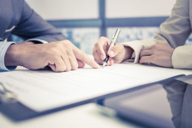 Two individuals in business attire reviewing and signing a document on a glass table.