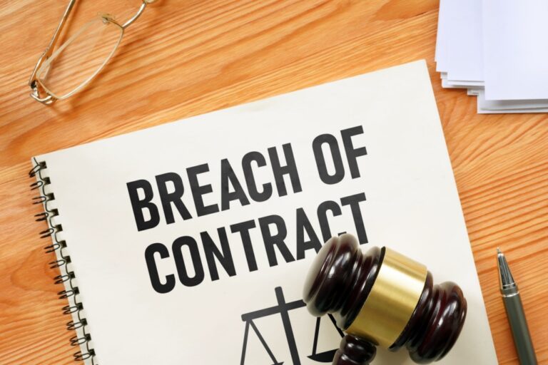 Spiral-bound document titled "BREACH OF CONTRACT" with a wooden gavel, pen, glasses, and papers on a wooden desk.