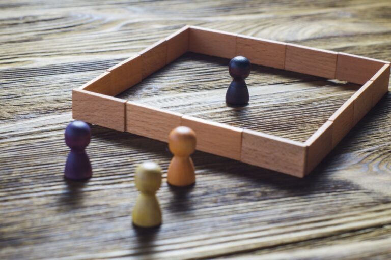 Wooden game pieces in various colors with one inside a square wooden frame on a textured wooden surface.