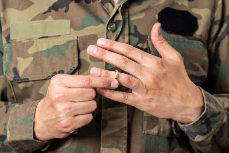 Close-up of a person in camouflage uniform removing a gold wedding ring from their finger.