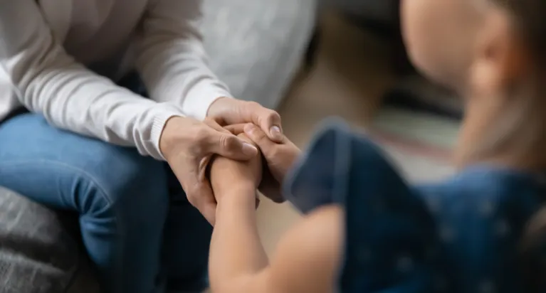 Adult in white long sleeve shirt holding child's hands, child in blue dress.