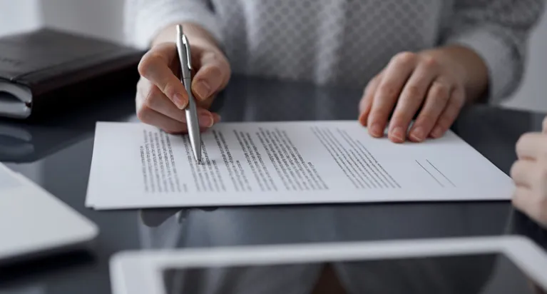 Person pointing at printed document with pen on reflective black table surface.