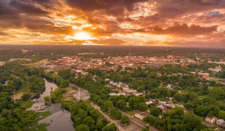 Aerial view of a town with dense greenery and a river under a dramatic sunset sky.